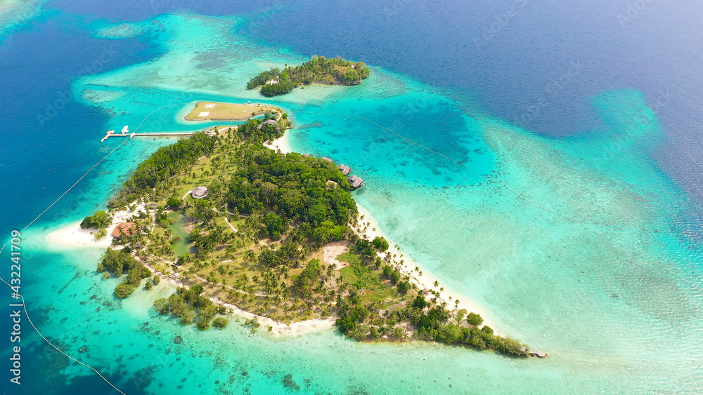 Aerial drone of Seascape with beautiful beach and tropical Malipano island with palm trees by coral reef from above. Philippines, Samal.