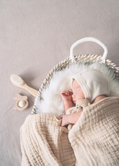 Sleeping newborn baby in basket wrapped in blanket in white fur background. Portrait of little child one week old with soft toys.