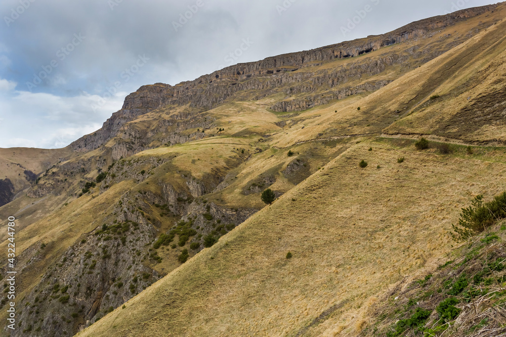 Panoramic view of Table Mountain in Ingushetia, Russia. Mountain landscape, rocks, plateau and cloudy sky. The road to the top. Mountain climbing. Tourist adventure. Dry alpine herbs Panoramic view of Table Mountain in Ingushetia, Russia. Mountain landscape, rocks, plateau and cloudy sky. The road to the top. Mountain climbing. Tourist adventure. Dry alpine herbs