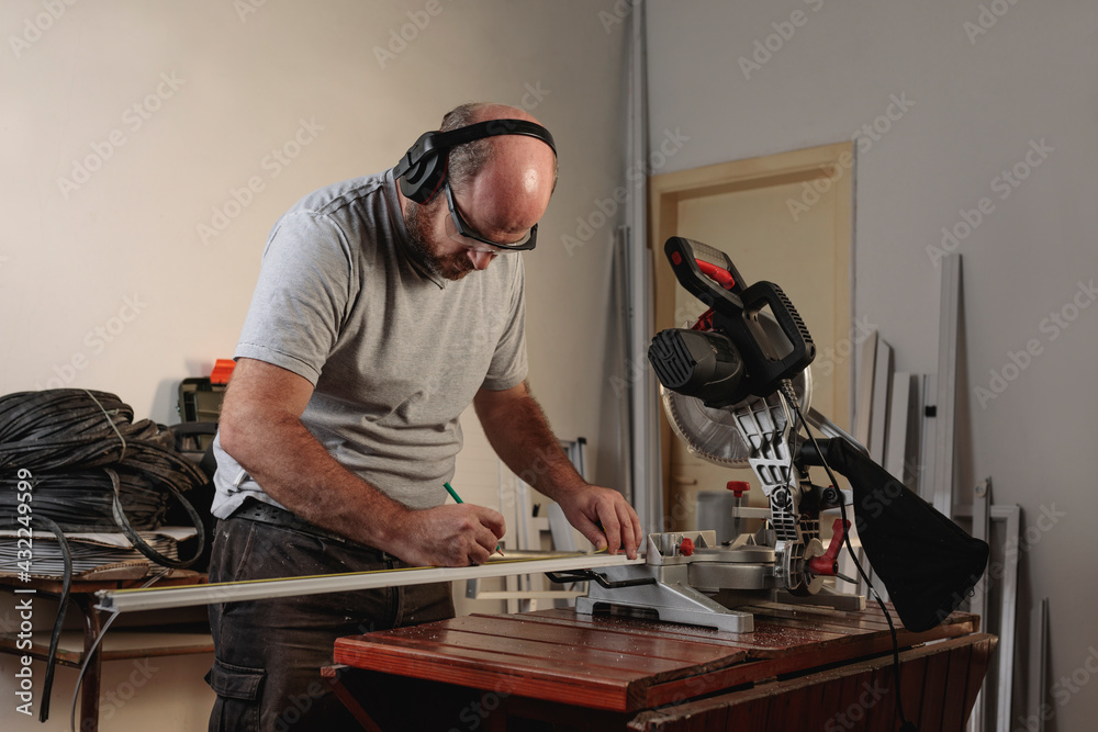 Man in a carpentry shop measuring white aluminum profile with tape measure. Profile to make a mosquito net Man in a carpentry shop measuring white aluminum profile with tape measure. Profile to make a mosquito net