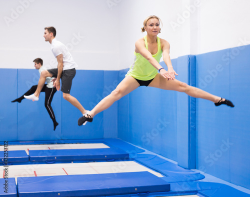 Young sporty woman with friends practicing and jumping in trampoline center © JackF