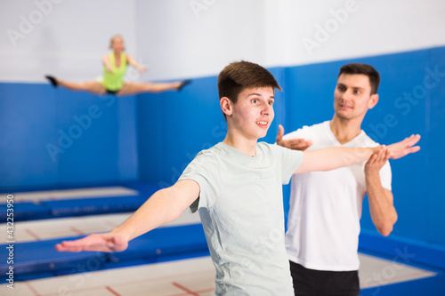 Skilled coach holding training with teenager in trampoline room, explaining basic jumping tricks..