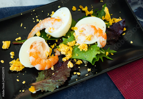 Huevos mimosa con gambas, eggs with prawns and salad on a black ceramic plate in a restaurant