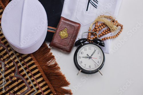 Flat lay of muslim dressed and accessories for salat with Holy Book of Al Quran and prayer beads and clock showing Duha time pray. There is Arabic word which means Holy Book photo