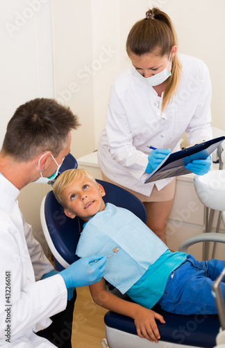 Male dentist with assistant are diagnosticating to young patient which is sitting in dental clinic.
