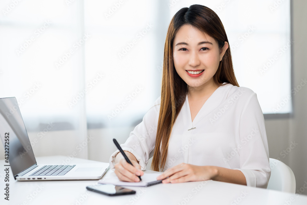 Young asian beautiful business woman working with laptop sitting at home and note on book. Smiling charming happy young female doing homework meeting conference with team at home. Young asian beautiful business woman working with laptop sitting at home and note on book. Smiling charming happy young female doing homework meeting conference with team at home.