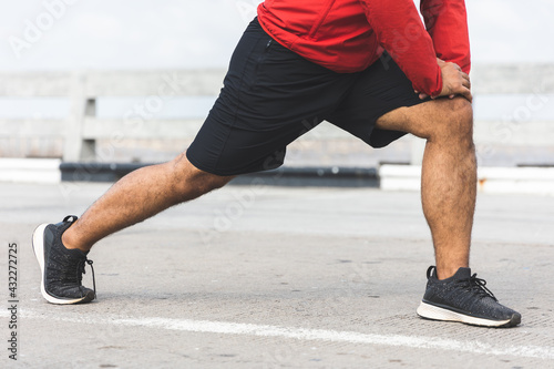 Young asian man wearing sportswear running outdoor. Portraits of Indian man stretching leg before running on the road. Training athlete work out at outdoor concept.