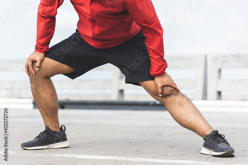 Young asian man wearing sportswear running outdoor. Portraits of Indian man stretching leg before running on the road. Training athlete work out at outdoor concept.