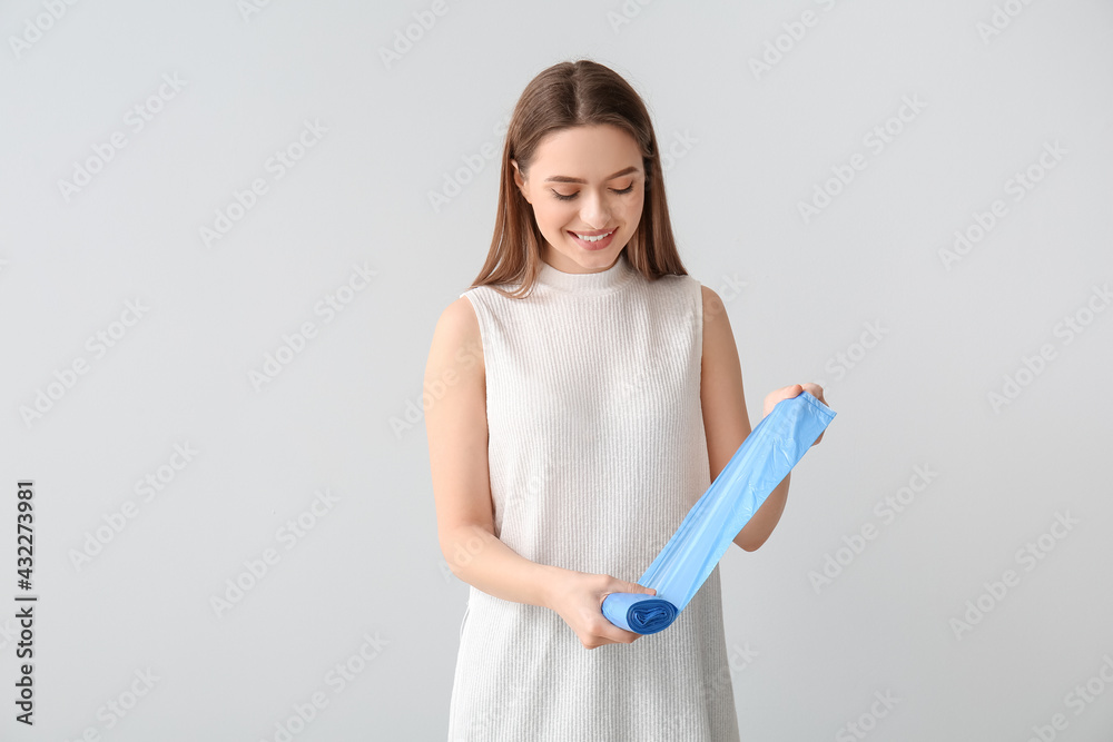 Young woman with garbage bags on light background