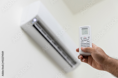 The young man used remote turn on the air conditioning . Adjust the temperature to cool. In the living room at home