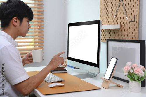 Side view young man holding coffee cup and pointing on screen of computer.