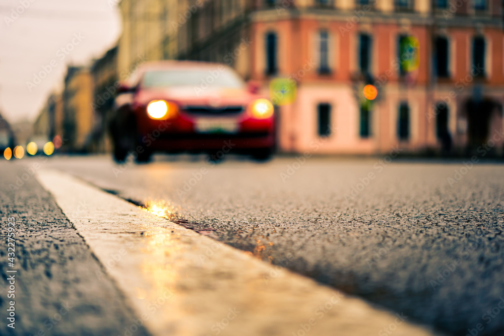 Rainy day in the big city, the red car rides ahead on the road. Close up view from the level of the dividing line Rainy day in the big city, the red car rides ahead on the road. Close up view from the level of the dividing line