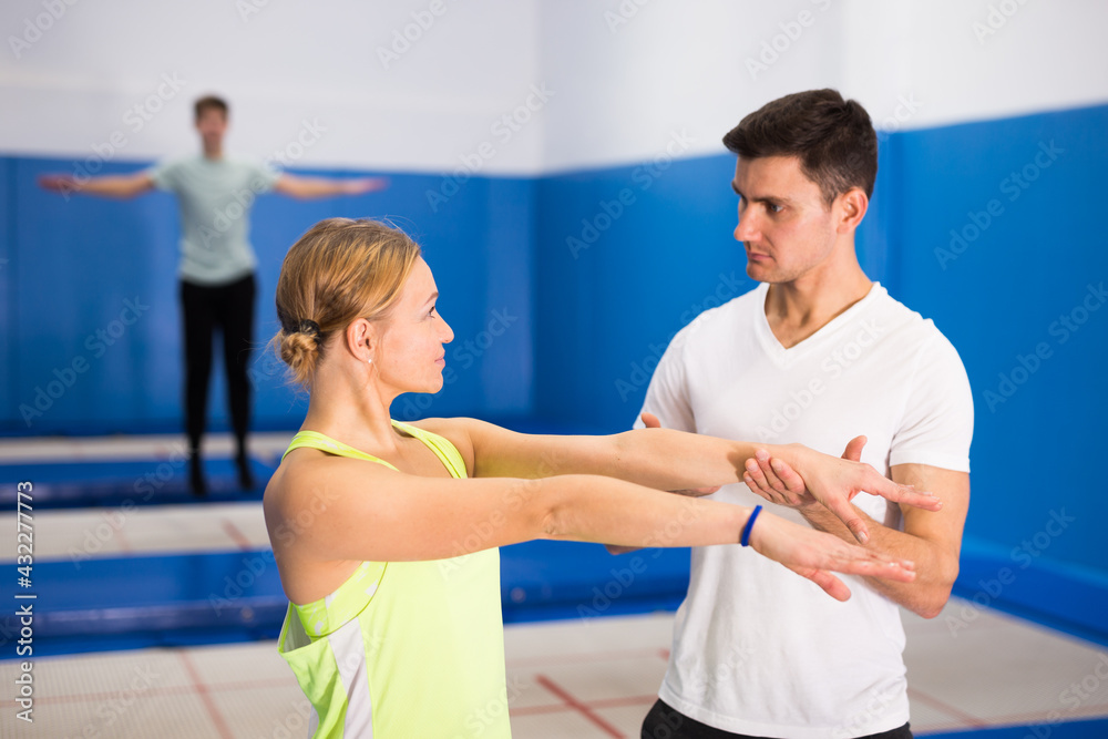 Obraz premium Portrait of man coach showing young woman jumping movements during trampoline training in sports center