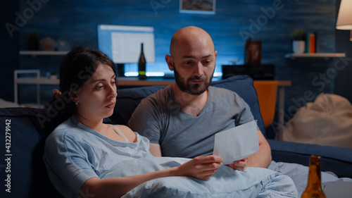 Shocked, worried frustrated, confused, desperate young couple reading eviction notice in paperwork letter feeling helpless. Unhappy tenants receving warning notification for unpaid bank bills photo