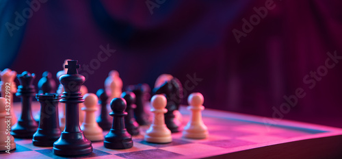 Print op canvas Chess pieces on a chessboard on a dark background shot in neon pink-blue colors