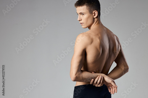 a man with pumped up muscles holds his hands behind his back on a gray background and behind Model 