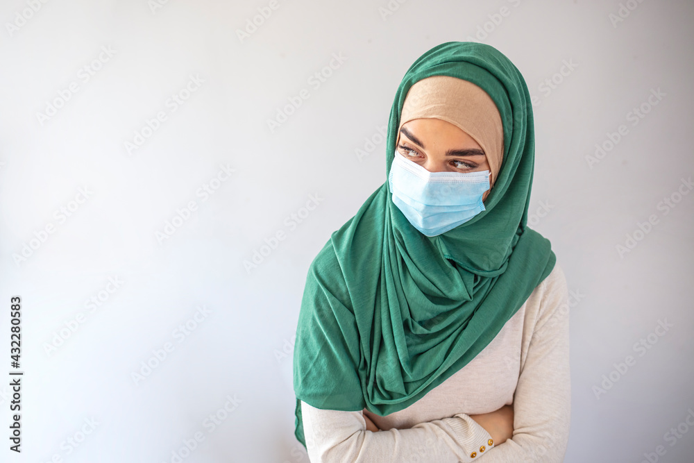 Young Muslim Arab female doctor healthcare worker or patient in hijab and protective face mask standing isolated over the gray background and looking at the camera, mockup image for advertisement Young Muslim Arab female doctor healthcare worker or patient in hijab and protective face mask standing isolated over the gray background and looking at the camera, mockup image for advertisement