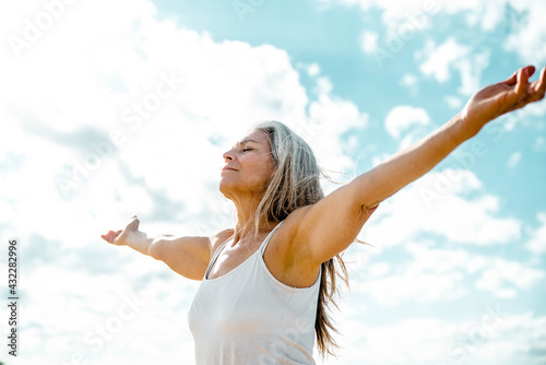 Joyful senior woman enjoying freedom standing with open arms and a happy smile looking up towards the sky - People and happiness concept