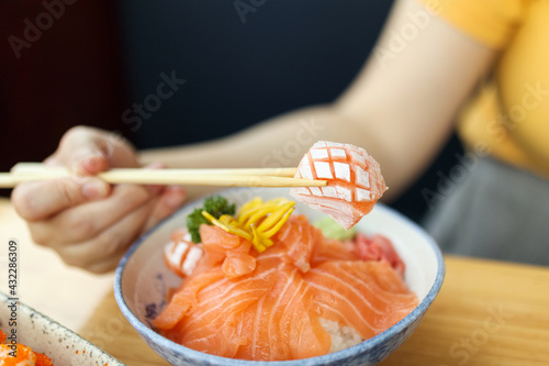 Asian woman eating salmon slice sashimi with rice in Japanese restaurant