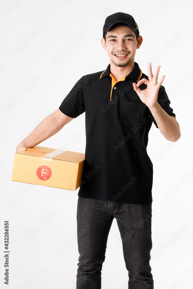 Smiling Asian delivery man makes OK gesture while holding package in right hand. Studio portrait of courier guy in black uniform on isolated white background. E-commerce business concept. Smiling Asian delivery man makes OK gesture while holding package in right hand. Studio portrait of courier guy in black uniform on isolated white background. E-commerce business concept.