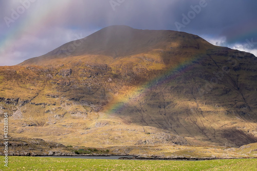 Rainbow in a mountains. Connemara  county Galway  Ireland. Green grass field in foreground  mountain in the background. Nobody. Irish landscape. Cloudy sky
