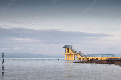 Blackrock public diving board. Salthill beach, Galway city, Ireland. Popular town landmark and swimming place. Calm morning light and blue cloudy sky, High tide
