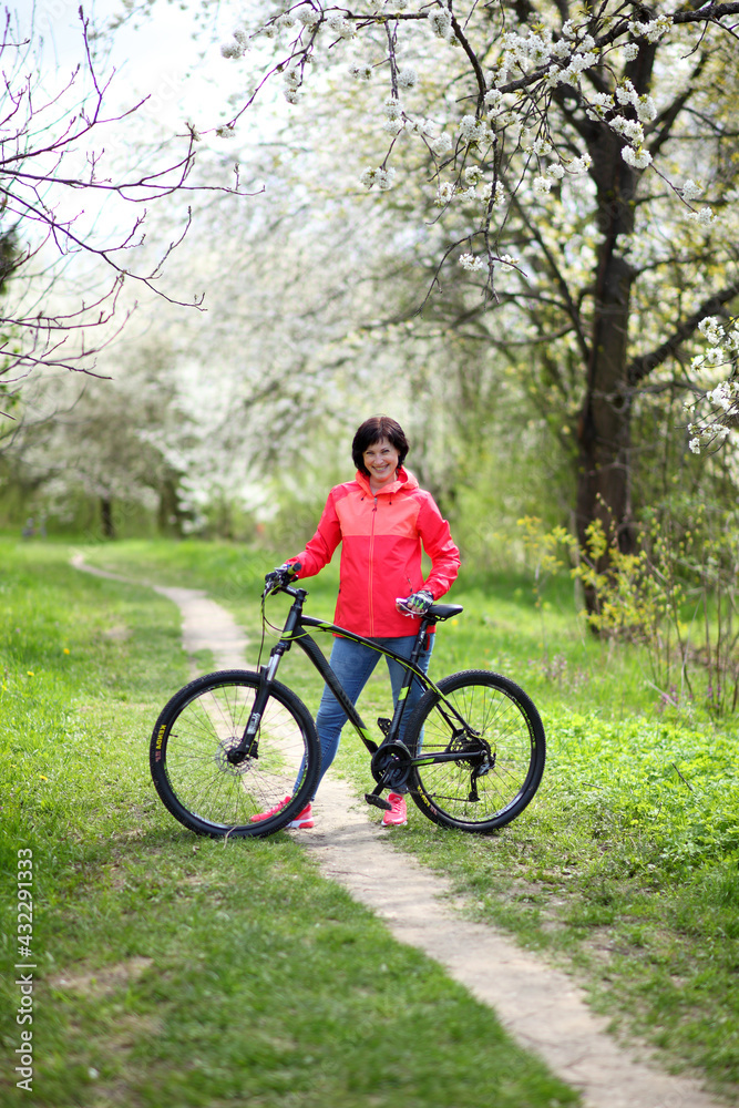 Beautiful woman on a bike in a blooming spring garden. Beautiful mature woman posing for the camera in a blooming spring garden.