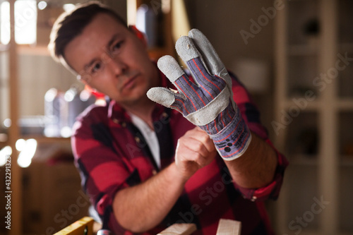Young male carpenter working in workshop. Carpenter putting on protective gloves