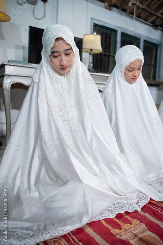 asian muslim family praying jamaah together at home. sholat or salah wearing white and hijab
