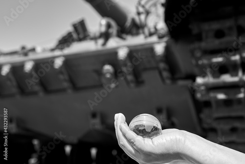 The glass globe of planet Earth in a woman's hand under the tracks of the tank. photo