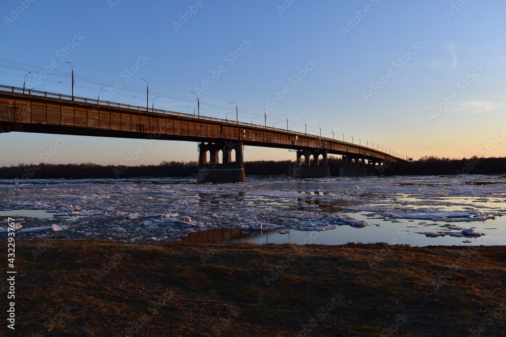 Beautiful evening landscape at sunset with a view of the bridge over the river during the spring ice drift.