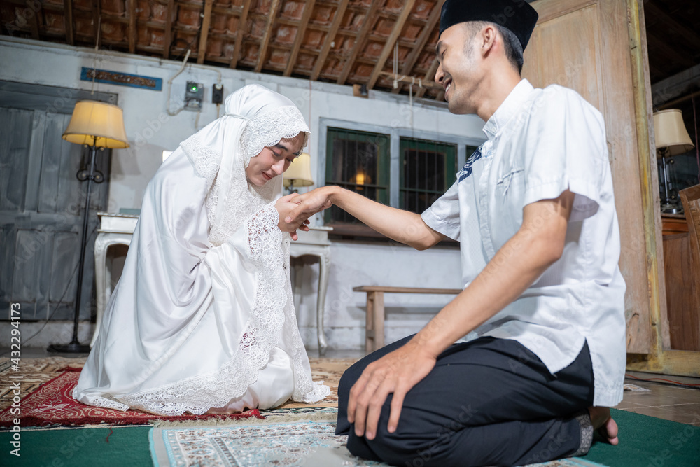 portrait of wife kissing her husband's hand after praying together at home. sholat or salat