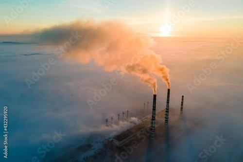 Aerial view of coal power plant high pipes with black smoke moving up polluting atmosphere at sunrise.