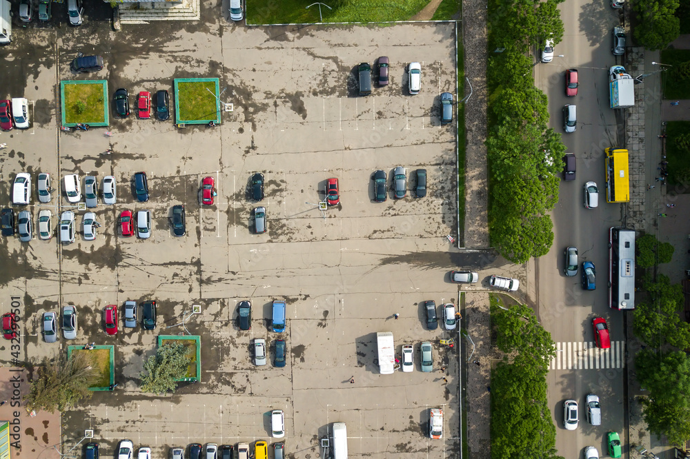 Obraz premium Top down aerial view of busy street with moving cars traffic and big parking lot with many parked vehicles.