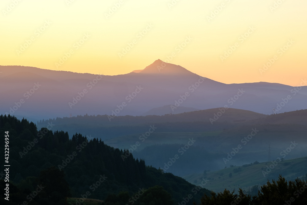 Beautiful mountain landscape with hazy peaks and foggy valley at sunset.