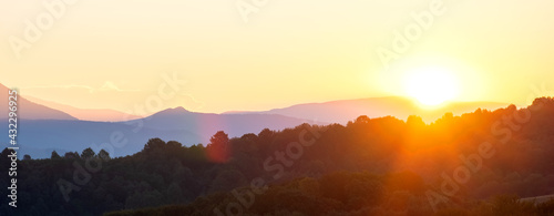 Panoramicl mountain landscape with hazy peaks and foggy wooded valley at sunset.