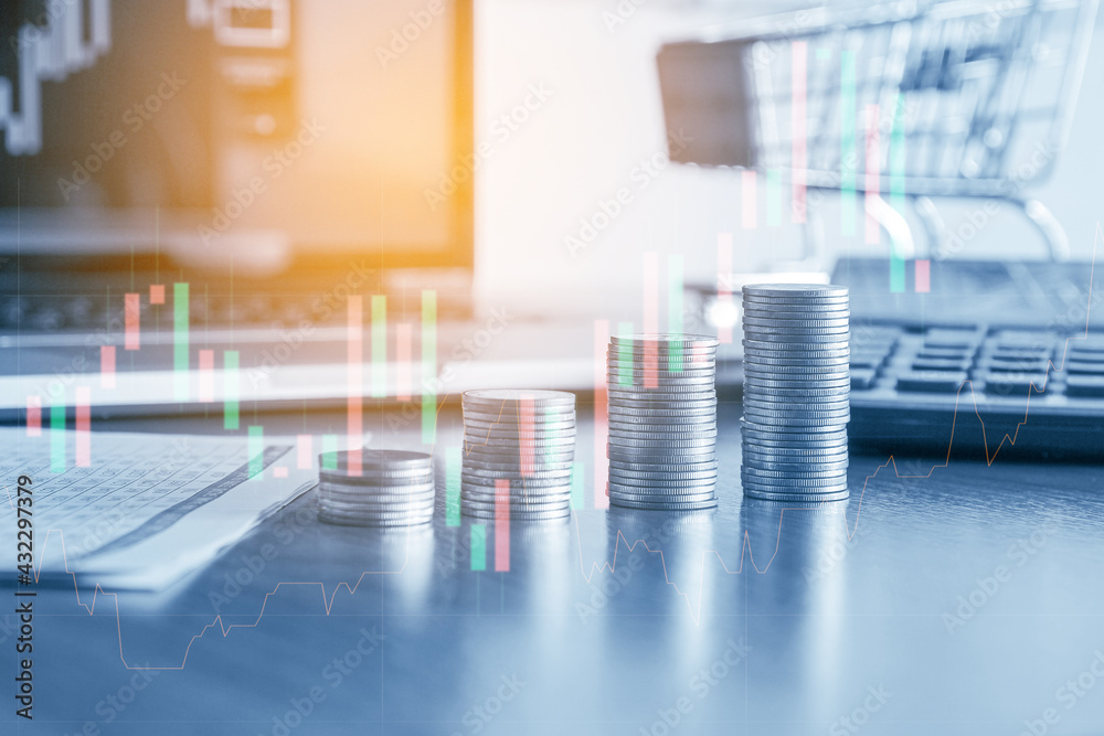 Stack of money coin with small shopping cart and laptop computer open trading graph in the background, Business and Financial concept. Stack of money coin with small shopping cart and laptop computer open trading graph in the background, Business and Financial concept.