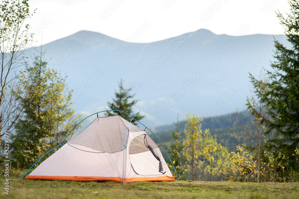 Empty hikers tent standing on campsite with view of majestic high mountain peaks in distance. Camping in wild nature and active travelling concept.