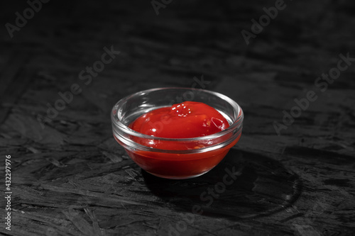 Glass bowl with ketchup close-up on a black background.