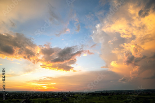 Dramatic sunset rural landscape with puffy clouds lit by orange setting sun and blue sky.
