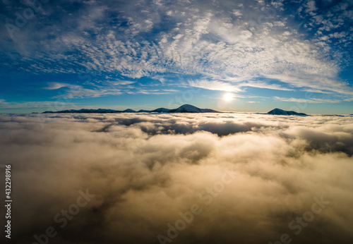 Aerial view of vibrant sunrise over white dense clouds with distant dark mountains on horizon.