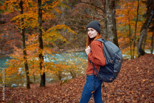 woman with backpack walking in the autumn park near the river in nature side view