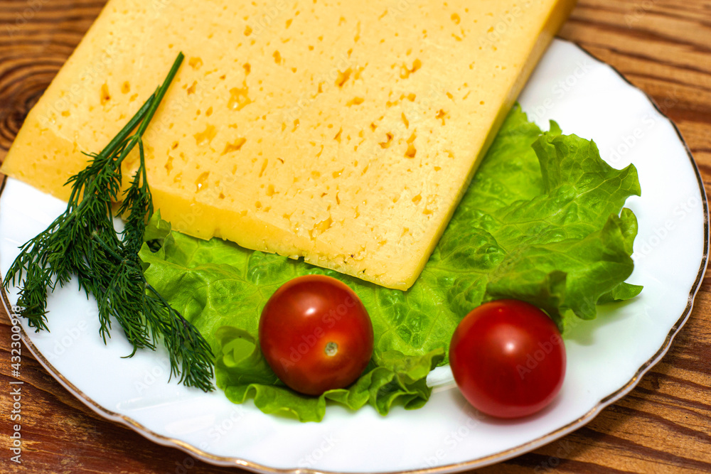 a large piece of cheese lettuce cherry tomatoes and herbs on a white plate on a wooden table a large piece of cheese lettuce cherry tomatoes and herbs on a white plate on a wooden table