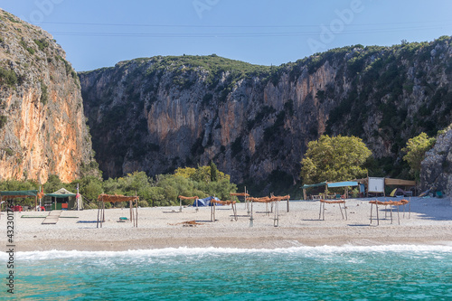A beautiful coast with sunshades and tents surrounded by cliffs and green trees and a turquoise sea, Gjipe Beach, Albania. Travel theme, beautiful nature