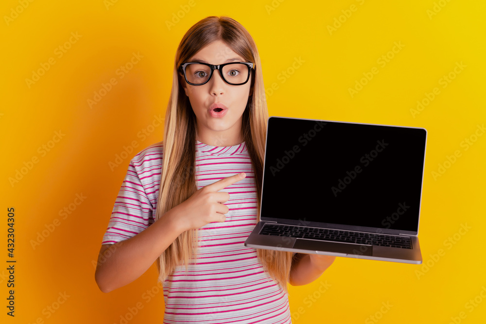 Photo of surprised child show point finger laptop touchscreen isolated over yellow background