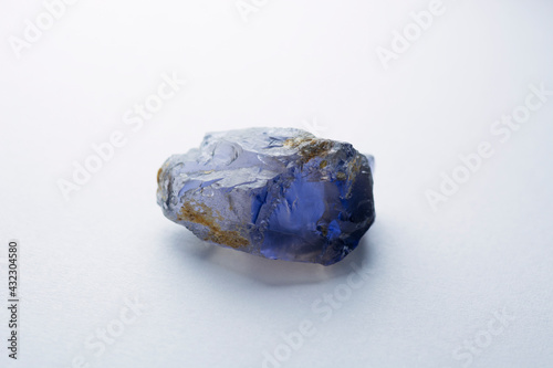 Natural raw rough tanzanian iolite blue violet color crystal specimen unfaceted gemstone. For faceting, lapidary or collection. Light gray gradient background. Gemology theme. Back light. photo