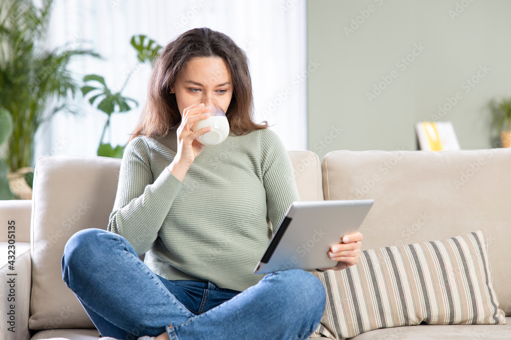 Young woman busy browsing tablet while drink a glass of milk. Young woman busy browsing tablet while drink a glass of milk.