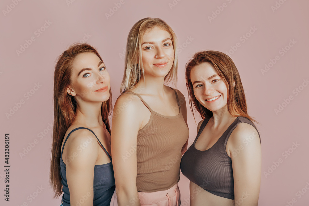 Three girls in comfortable home clothes together on a pink background. Women smile and have fun. The concept of spa treatments, natural beauty and care, youth, cream and mask, freshness, friendship Three girls in comfortable home clothes together on a pink background. Women smile and have fun. The concept of spa treatments, natural beauty and care, youth, cream and mask, freshness, friendship