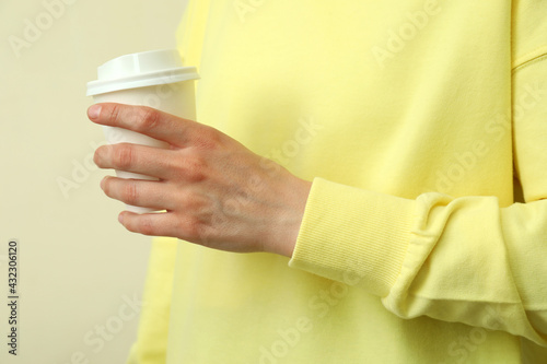 Young woman in yellow sweatshirt hold paper glass against beige background