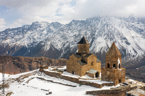 Scenic mountainous landscape with medieval Gergeti Trinity Church and belfry on background with snow covered Mount Kazbegi on spring day, Georgia. photo
